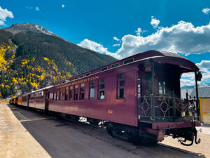 Durango train car parked at the Silverton train station with fall colors in the background