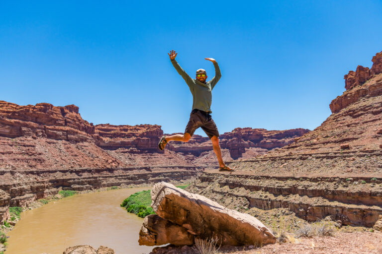 Man jumping into the air with the Colorado River in the background in Cataract Canyon, Utah