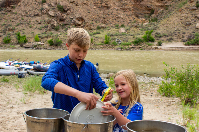 Brother showing sister how to wash dishes on a river trip in Desolation Canyon