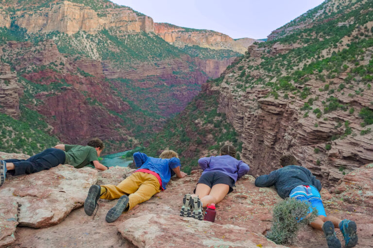 Four kids laying down looking over the edge of a cliff at the Hanging Gardens Overlook in Gates of Lodore - Mild to Wild