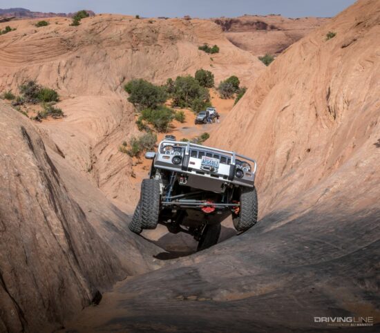 Jeep with one tire in the air going up the sandstone of Hell's Revenge trail in Moab