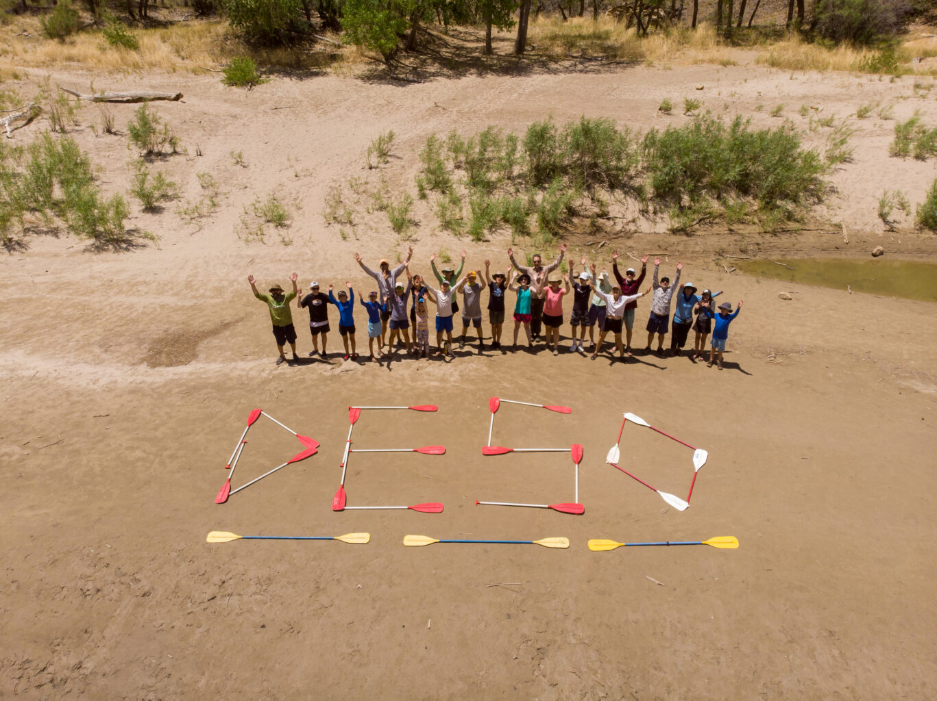 Group shot with Deso spelled out in paddles on the beach - Mild to Wild