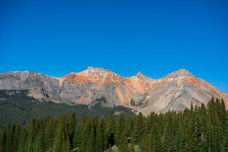 Wide view of the San Juan Mountains with trees in front of the orange hued mountains