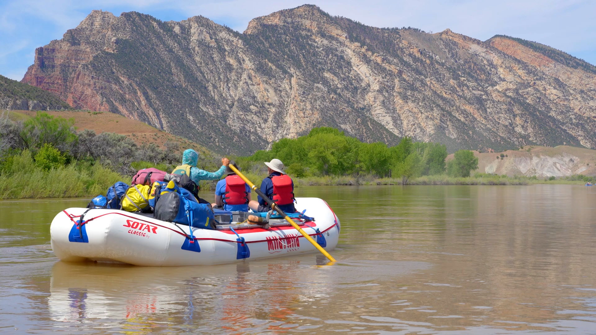 medium shot of a raft on the yampa river with guests on the boat and beautiful faults in the background