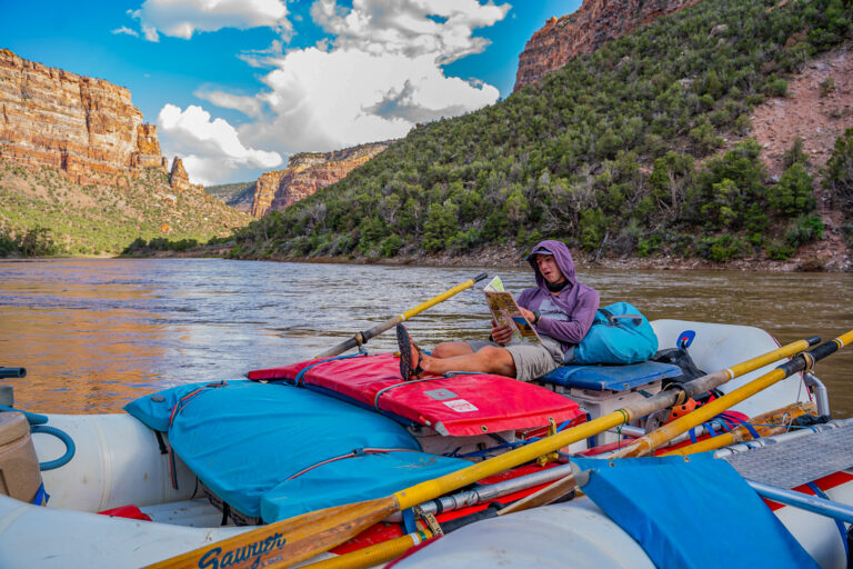 Guide reading the Yampa River map while lounging on his boat at camp - Mild to Wild